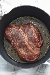 A chuck roast searing inside a cast iron skillet.